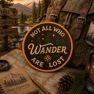 May include: A brown patch with the text "NOT ALL WHO WANDER ARE LOST" and a compass design, set against a backdrop of a backpack, map, compass, and a lantern. The patch features a forest design and is surrounded by a yellow border.
