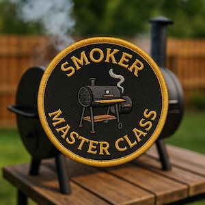 May include: Embroidered patch with the words "SMOKER MASTER CLASS" in gold lettering on a black background. The patch features a detailed illustration of a smoker grill. The patch is round with a gold border.