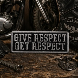 May include: A rectangular black embroidered patch with a gray border and the text GIVE RESPECT GET RESPECT in gray capital letters. The patch features a clean, stitched finish and is designed for application to fabric surfaces like jackets or vests.