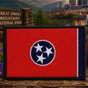 May include: A rectangular embroidered patch featuring the Tennessee state flag design. The patch has a red field with a central blue circle containing three white stars, bordered by a thin white stripe and a dark blue vertical bar on the right side.
