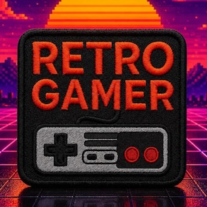 Puede incluir: Un parche bordado cuadrado con fondo negro que presenta el texto naranja RETRO GAMER sobre un gráfico de mando de juego gris y negro con dos botones rojos. El parche tiene un borde negro grueso y esquinas redondeadas.