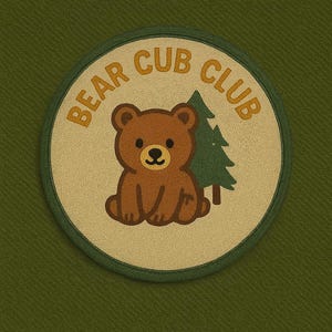 May include: A circular patch with the words "BEAR CUB CLUB" in gold lettering. The patch features a brown bear cub and a green pine tree on a beige background, all set against a green fabric.