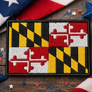 May include: Embroidered patch featuring the Maryland state flag, with a black border. The flag design includes a black and yellow pattern, and red and white crosses. Patriotic stars and a flag are in the background.