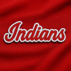 May include: A red fabric with the word "Indians" embroidered in white and red cursive lettering. The word is outlined in white thread, creating a raised effect. The background is a solid, textured red.