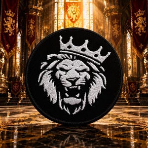 May include: A circular black embroidered patch featuring a white lion head wearing a crown. The lion is depicted with a roaring expression, detailed mane, and sharp features. The embroidery is dense and textured, creating a high-contrast design.
