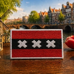 May include: A rectangular embroidered patch featuring the flag of Amsterdam, which consists of a horizontal red, black, and red striped design with three white Saint Andrew's crosses centered horizontally within the black band.