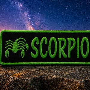 May include: A black rectangular patch with a green border and the word "SCORPIO" in green, stylized, textured lettering. A green scorpion graphic is on the left. The patch is set against a background of a starry night sky.
