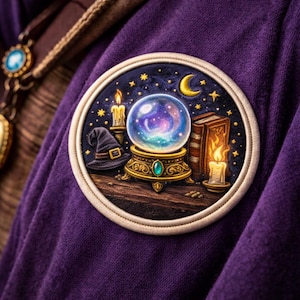 May include: A round patch featuring a crystal ball, a witch's hat, a book, and candles against a starry night sky. The patch has a gold and blue color scheme with a cream-colored border. The patch is on a purple fabric.