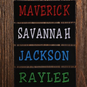 May include: Four black embroidered name patches with different names. The top patch reads "MAVERICK" in red, the second reads "SAVANNAH" in white, the third reads "JACKSON" in blue, and the bottom reads "RAYLEE" in green.