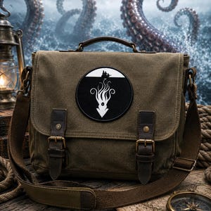 May include: An olive green canvas messenger bag with a top handle and adjustable shoulder strap. The front flap features two brown leather buckle straps and a circular patch depicting a white silhouette of a kraken beneath a small boat.