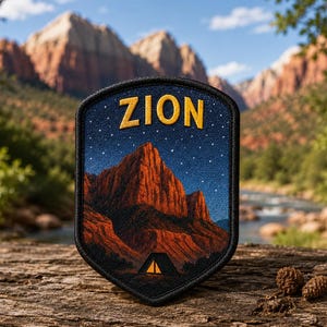 May include: A black patch with the word "ZION" in gold lettering. The patch features a night sky with stars above a mountain range and a tent. The patch is on a wooden surface with a scenic background.