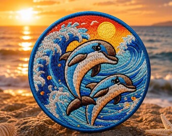 Op de afbeelding: Een ronde geborduurde patch met twee dolfijnen die door blauwe oceaangolven springen tegen een achtergrond van een zonsondergang met een gele zon. Het ontwerp bevat blauwe, witte, oranje en gele draden en is afgewerkt met een blauwe rand.
