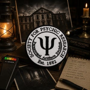 May include: A circular embroidered patch with a white background and black border. The text reads SOCIETY FOR PSYCHIC RESEARCH, Paranormal Artifacts Division, and Est. 1882. A large black Greek letter Psi symbol is centered in the middle of the patch.