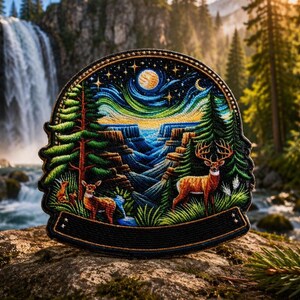 Pode incluir: Um emblema bordado circular com uma paisagem detalhada de um desfiladeiro, árvores perenes e dois veados. A cena é apresentada sob um céu noturno com lua e estrelas, emoldurada por uma borda preta com um espaço retangular vazio na base.