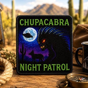 May include: A square embroidered patch with a black border featuring the text CHUPACABRA NIGHT PATROL in green. The design depicts a dark creature with glowing red eyes, a silhouette of a coyote, a cactus, a full moon, and a UFO in the night sky.