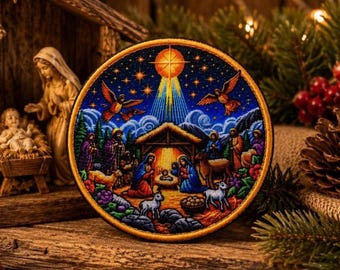 May include: A circular embroidered patch featuring a colourful nativity scene. The design depicts a central stable with figures, animals, and a bright star above, all set against a deep blue starry sky with two flying angels in the upper section.