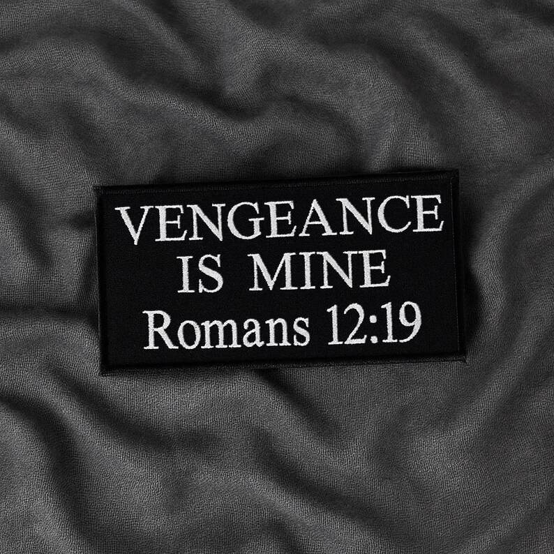 Op de afbeelding: Een zwart rechthoekig embleem met wit geborduurde tekst. De tekst luidt "VENGEANCE IS MINE Romans 12:19". De patch is geplaatst tegen een grijze, getextureerde achtergrond.