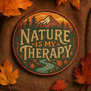Könnte beinhalten: Runder, gestickter Aufnäher mit dem Text "NATURE IS MY THERAPY". Das Design zeigt einen Berg, Bäume und einen Fluss, mit Herbstblättern am Rand. Die Farbpalette umfasst Grün-, Orange- und Brauntöne.