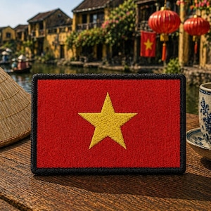 May include: A rectangular embroidered patch featuring the flag of Vietnam, which consists of a solid red background with a large, centered five-pointed yellow star. The patch has a thick, black stitched border surrounding the entire rectangular edge.