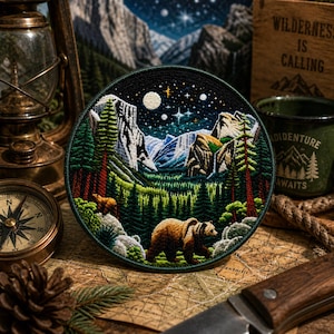 May include: Round embroidered patch depicting a mountain scene with a bear, trees, and a starry night sky. The patch has a dark green border. The design includes a bear, trees, mountains, and a night sky with a moon and stars.