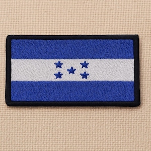 Puede incluir: Parche bordado con la bandera de Honduras. El diseño incluye un campo azul, una franja blanca y cinco estrellas azules. El parche tiene un borde negro y es de forma rectangular.