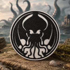 May include: A circular embroidered patch featuring a black and white graphic design of a stylized cephalopod creature with tentacles and wings. The patch has a thick white border and a black background with white line art details throughout.