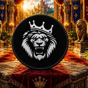 Può includere: Una toppa circolare nera con un disegno ricamato in bianco di un leone ruggente che indossa una corona. La criniera del leone è dettagliata con linee stilizzate e nitide, e la corona è posizionata in modo prominente sulla testa. La toppa ha un bordo cucito.