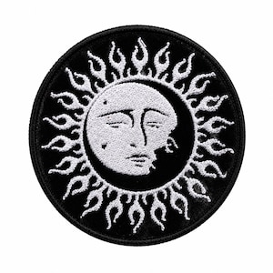 May include: A circular embroidered patch featuring a white sun face with closed eyes and a crescent moon silhouette on a black background. The sun is surrounded by white flame-like rays extending towards the black stitched border edge.