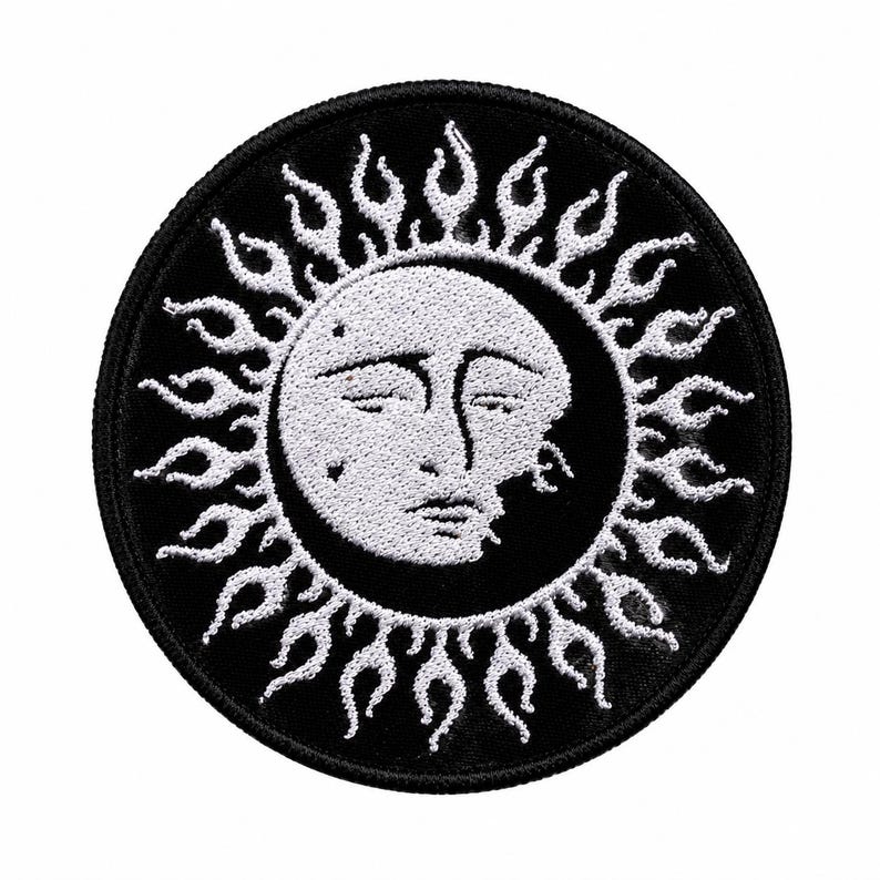 May include: A circular embroidered patch featuring a white sun face with closed eyes and a crescent moon silhouette on a black background. The sun is surrounded by white flame-like rays extending towards the black stitched border edge.