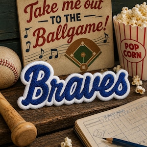 May include: A blue and white embroidered "Braves" patch is the focal point, set against a baseball-themed backdrop. A baseball, popcorn, a scorecard, and a sign that reads "Take me out to the Ballgame!" complete the scene.