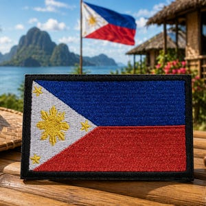 May include: Embroidered patch featuring the flag of the Philippines. The flag has a blue upper half, a red lower half, and a white triangle with a yellow sun and three stars. The patch is rectangular with a black border.