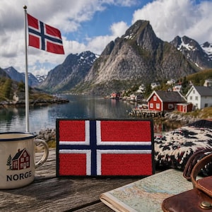 May include: A rectangular patch of the Norwegian flag, red with a white-bordered blue cross. A mug with "Norge" and a house graphic is next to it. A Norwegian flag flies in the background, with mountains and a lake.