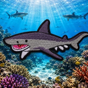 May include: An embroidered shark patch featuring a dark purple top, a light gray underbelly, and a wide open mouth with bright pink gums and white teeth. The shark is depicted in a swimming position with a black stitched border outline.