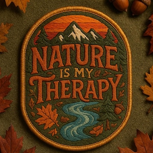Könnte beinhalten: Gestickter Aufnäher mit dem Text "NATURE IS MY THERAPY" in Orange. Der Aufnäher zeigt eine Berglandschaft, einen Fluss und Bäume. Braune und orangefarbene Blätter und Eicheln umgeben den Aufnäher auf grünem Hintergrund.