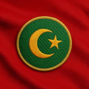 Puede incluir: Parche bordado circular con fondo verde, diseño de luna creciente y estrella doradas y ribete dorado. El parche está sobre un fondo de tela roja.