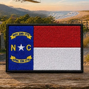 Puede incluir: Un parche rectangular bordado con la bandera del estado de Carolina del Norte. El diseño incluye una franja vertical azul con una estrella blanca entre las letras N y C, flanqueada por dos cintas amarillas con MAY 20th 1775 y APRIL 12th 1776.