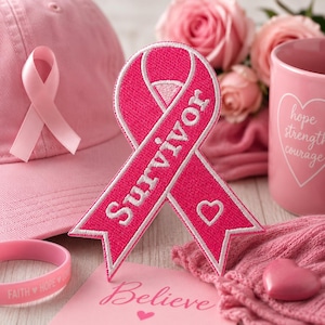 May include: A collection of pink items, including a baseball cap, a ribbon, a mug, a bracelet, and a heart-shaped object. The ribbon is embroidered with the word "Survivor" in white. The mug has a heart design and the words "hope strength courage".