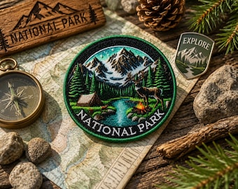 May include: A circular embroidered patch featuring a mountain landscape with a deer, a campfire, a tent, and a river. The text NATIONAL PARK is stitched in white along the bottom border. The design includes green pine trees and snow-capped peaks.