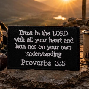 May include: A rectangular black patch featuring white embroidered text that reads: Trust in the LORD with all your heart and lean not on your own understanding Proverbs 3:5. The patch has a stitched border and a flat, fabric-like texture.