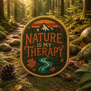 Könnte beinhalten: Ein runder, bestickter Aufnäher mit einer Berglandschaft, einem gewundenen Fluss, Tannen und Herbstblättern. Der Text "NATURE IS MY THERAPY" ist in orangefarbenen Buchstaben in die Mitte gestickt und von einem goldfarbenen Rand umgeben.