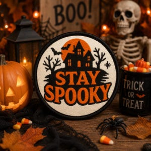 May include: A circular embroidered patch with a cream background featuring a black silhouette of a haunted house, bare trees, and bats against an orange moon. The text STAY SPOOKY is embroidered in bold orange letters across the center.