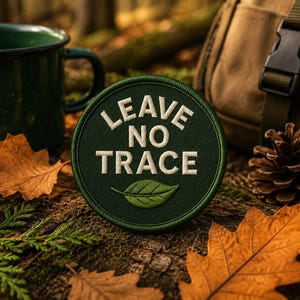 May include: A circular green patch with the words "LEAVE NO TRACE" in white, and a green leaf graphic. The patch is surrounded by fall foliage, a green mug, a backpack, and a pinecone.