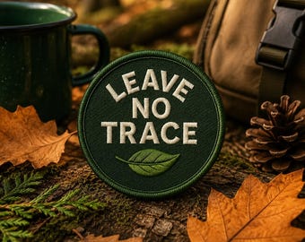 May include: A circular green patch with the words "LEAVE NO TRACE" in white, and a green leaf graphic. The patch is surrounded by fall foliage, a green mug, a backpack, and a pinecone.