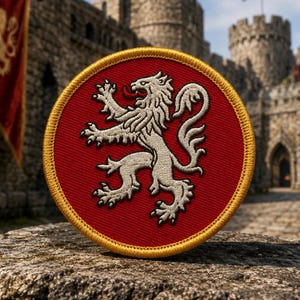May include: A circular embroidered patch featuring a red background with a gold border. In the centre, a white rampant lion is depicted with its tongue extended. The embroidery shows a textured thread pattern throughout the design.