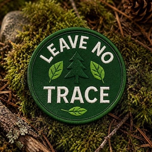 Peut inclure: Un écusson brodé circulaire vert foncé avec une bordure cousue blanche. Le texte LEAVE NO TRACE est brodé en lettres capitales blanches, entourant une icône de sapin centrale et trois petites feuilles vertes disposées autour.