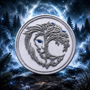 May include: A circular embroidered patch featuring a grey thread design of a lion head merged with a tree silhouette. The lion eye and two small accents are stitched in bright blue thread. The patch has a white fabric base and a stitched border.