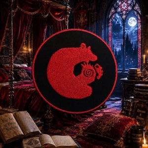 Puede incluir: Un parche bordado circular con un símbolo de dragón rojo sobre un fondo negro. El diseño muestra a un dragón mordiéndose la propia cola en un movimiento circular, con un patrón de espiral en el cuerpo. El parche tiene un borde rojo cosido.