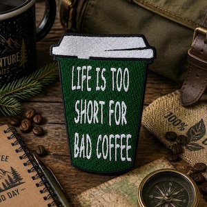 May include: A dark green embroidered patch shaped like a coffee cup with a white lid. The text "LIFE IS TOO SHORT FOR BAD COFFEE" is stitched in white capital letters across the center of the cup. The patch has a black border.