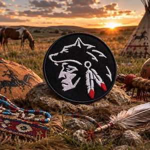 May include: A black embroidered patch with a Native American profile and a wolf head design, with white and red detailing. The image also shows a Native American headdress, a beaded necklace, and a teepee, set against a sunset.