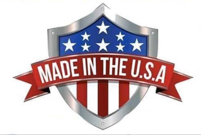 May include: A shield-shaped emblem featuring a metallic silver border and a blue field with white stars above red and white vertical stripes. A red ribbon banner overlays the center with the white text MADE IN THE U.S.A. printed across it.